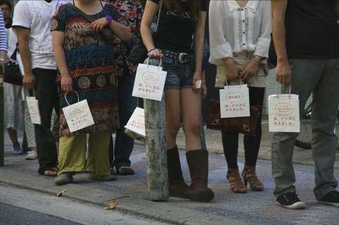 （写真1）、「私、○○（理由）だから、ジンズにかえました。」と書かれたショップバッグを持って行列をつくる人々。image by JINS