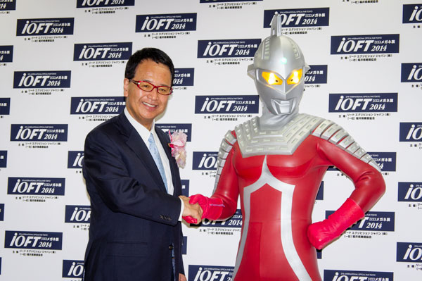 「めがねの聖地」とウルトラセブンとのコラボから生まれたメガネ「ウルトラセブン × ブラックアイズ」US701F-1 メタリックレッドを掛けた甘利大臣は、ウルトラセブンとガッチリ握手。 lang=